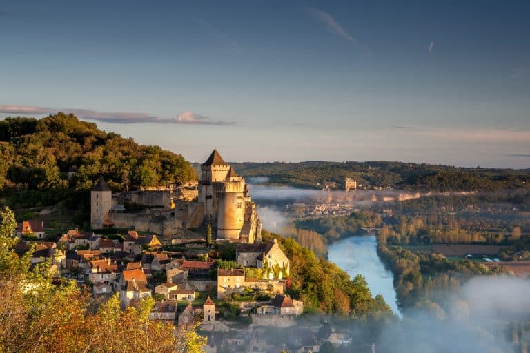 Château de Castelnaud la Chapelle ved solopgang med Dordgnefloden stille løb og Chateau de Beynac i baggrunden.